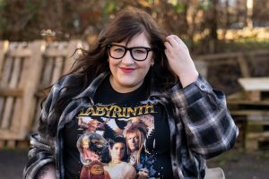 Woman in wheelchair smiling and holding hair back whilst wearing Labyrinth tshirt