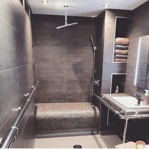 Dark grey/brown tiled walls and floors with tiled bench and hoist above shower. 
